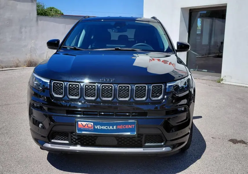 Vue frontale d'un Jeep Compass noir 2025 avec calandre distinctive et phares LED allumés, stationné en extérieur.
