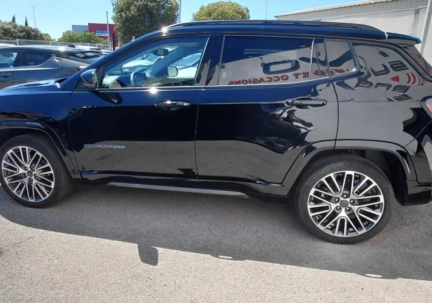 Jeep Compass noir vu de profil côté gauche, avec jantes alliage 19 pouces et barres de toit visibles.