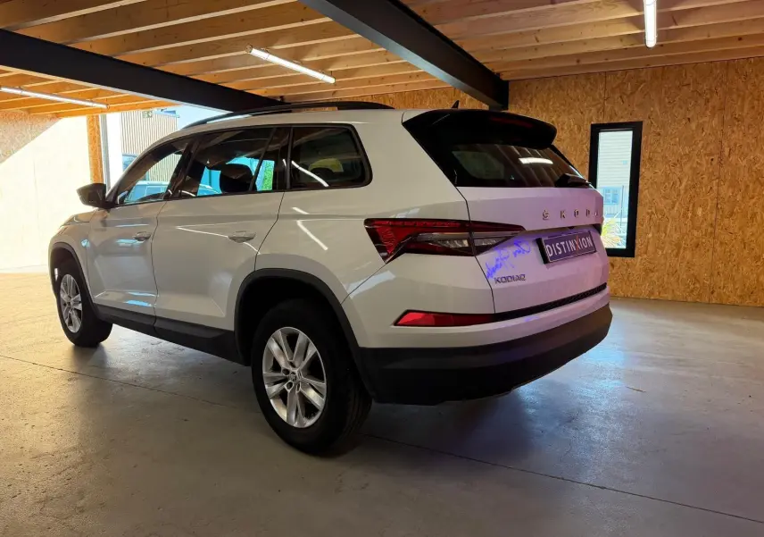 Vue intérieure côté gauche du Skoda Kodiaq blanc 2023, sièges avant en tissu noir et tableau de bord moderne.