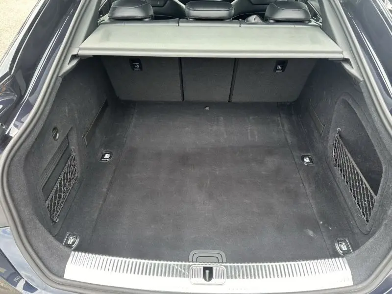 Coffre spacieux de l'Audi A5 Sportback bleu lunaire métal, vue arrière ouverte montrant les filets latéraux et la plage arrière.