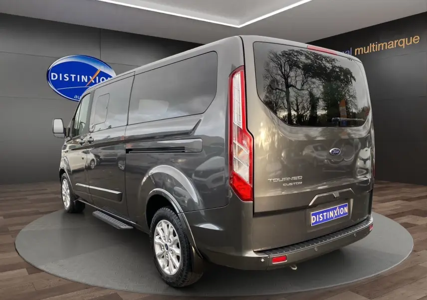 Vue 3/4 arrière droite d'un Ford Tourneo Custom gris magnetic avec hayon et vitres teintées en showroom.