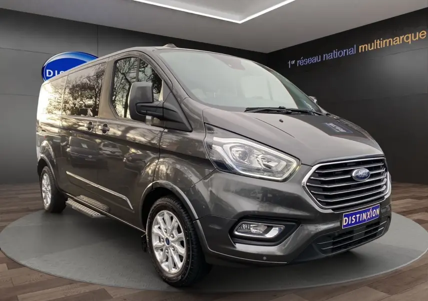 Ford Tourneo Custom gris Magnetic en 3/4 avant droit, avec calandre chromée et jantes alliage visibles.