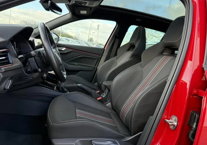 Vue intérieure côté gauche du Skoda Kamiq rouge velvet, sièges sport noirs avec bandes rouges et volant cuir multifonctions.