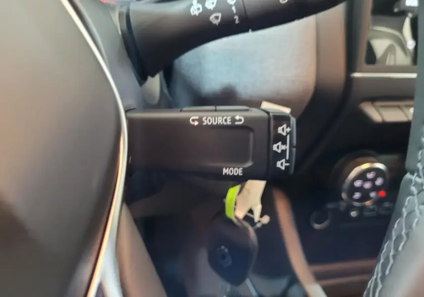 Gros plan sur la commande au volant de la Renault Clio gris foncé, avec détails des boutons source et mode.