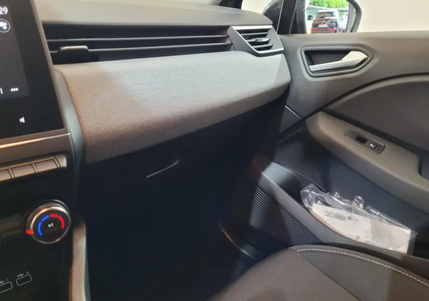 Vue intérieure côté passager de la Renault Clio gris foncé 2025, avec tableau de bord textile et commandes climatisation visibles.