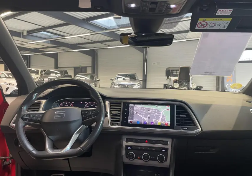 Vue intérieure frontale du tableau de bord du SEAT Ateca rouge 2022, avec écran tactile de navigation et volant multifonction.