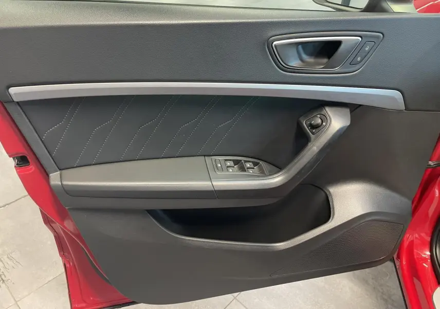 Détail de la porte côté conducteur du SEAT Ateca rouge 2022, montrant les commandes de vitres et la poignée intérieure.