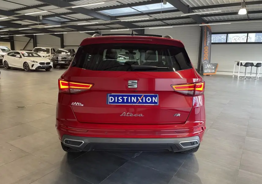 Vue arrière d'un SEAT Ateca rouge 2022 en finition FR, avec feux allumés dans un showroom lumineux.