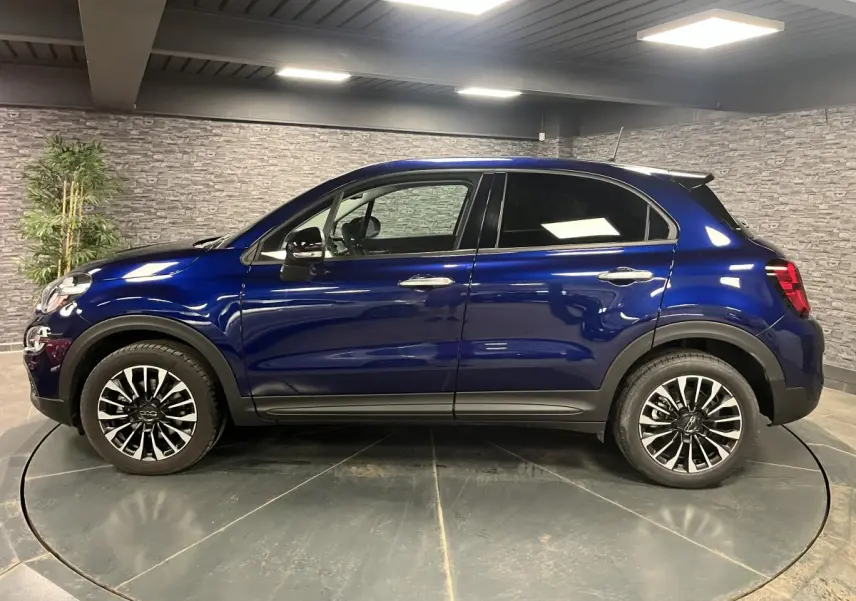 Profil latéral droit d'une Fiat 500X bleu métallisé avec jantes alliage 17 pouces dans un showroom.