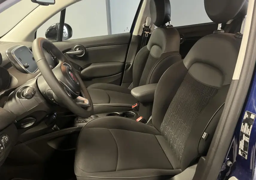 Vue intérieure côté conducteur de la Fiat 500X 2024, sièges tissu noir avec monogramme FIAT, volant Soft-Touch visible.