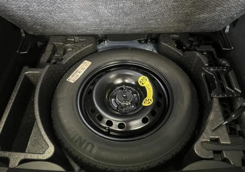 Vue en plongée sur la roue de secours noire dans le coffre d'une Fiat 500X bleu 2024.