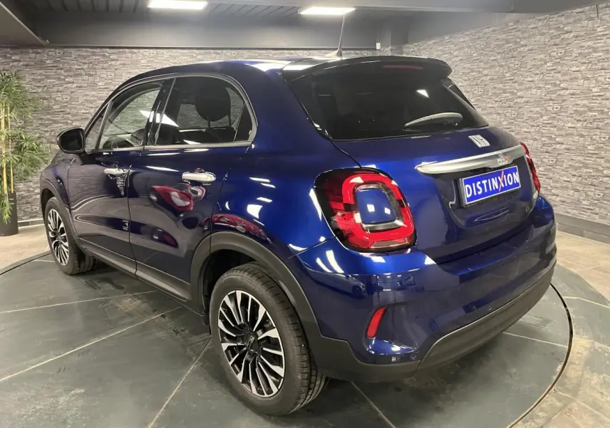 Vue 3/4 arrière droite d'un Fiat 500X bleu métallisé avec jantes alliage 17'' et vitres surteintées.