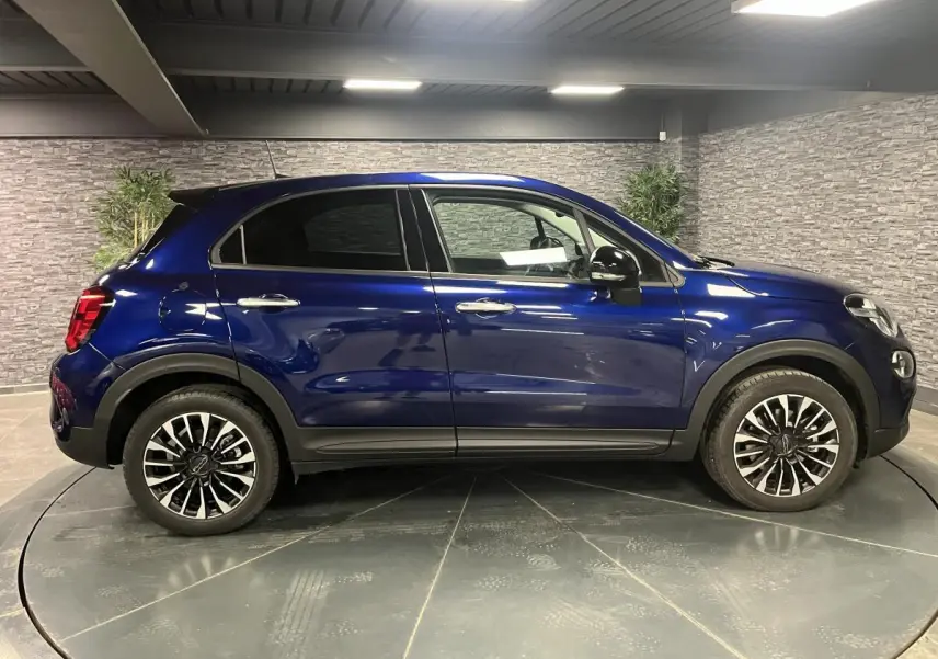 Vue de profil côté gauche d'un Fiat 500X bleu métallisé avec jantes alliage 17 pouces dans un showroom.