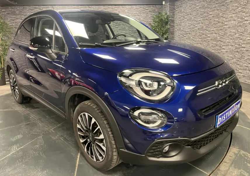 Fiat 500X bleu métallisé vue 3/4 avant droit avec jantes alliage 17'' et phares LED dans un showroom.
