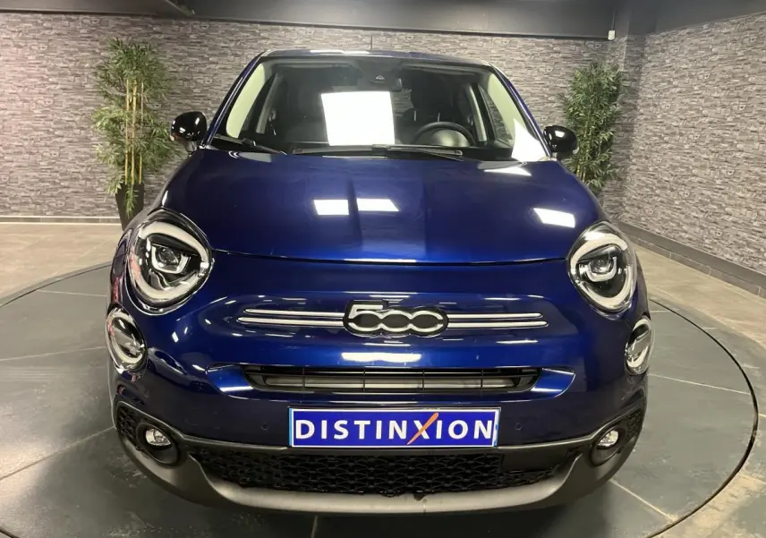 Vue frontale d'une Fiat 500X bleu métallisé avec logo 500 distinctif et phares LED dans un showroom.
