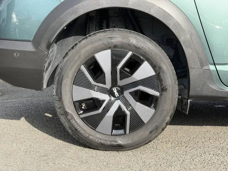 Gros plan sur la roue avant gauche du Dacia Jogger 2025 Vert Cèdre métallisé avec jante au design géométrique noir et gris.