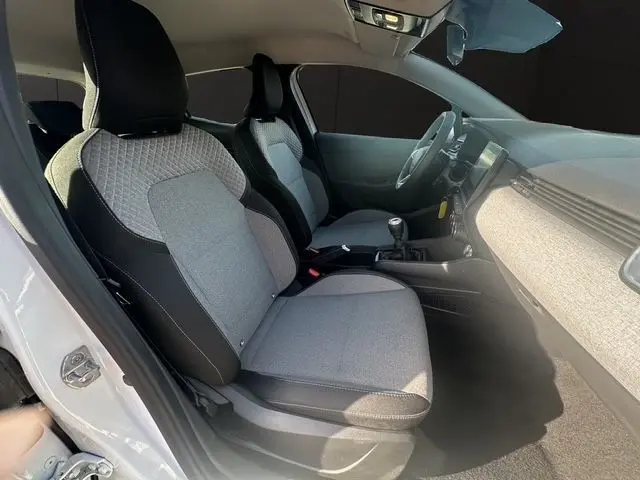 Vue intérieure côté conducteur de la Renault Clio blanche 2025, sièges tissu gris et tableau de bord moderne.