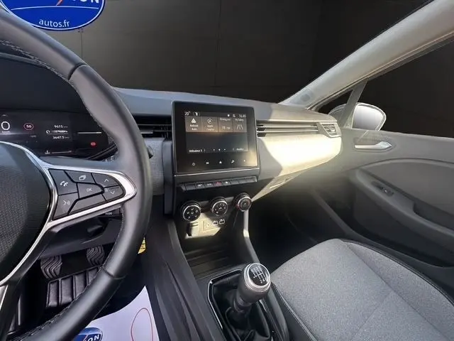 Vue intérieure de la Renault Clio blanche 2025 montrant le volant multifonctions, écran tactile central et levier de vitesse manuel.