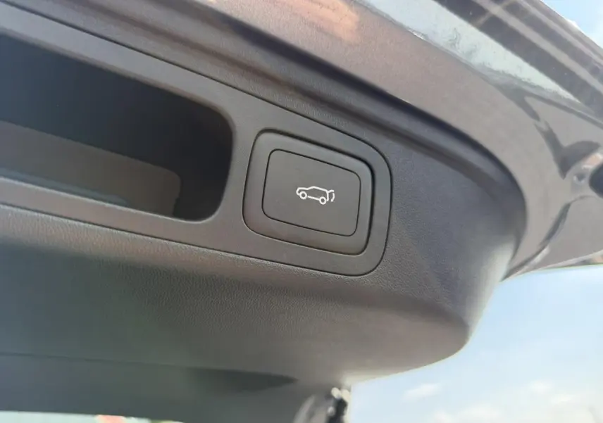 Bouton d'ouverture électrique du hayon sur le bord intérieur du coffre d'un MG Motor EHS gris métallisé.