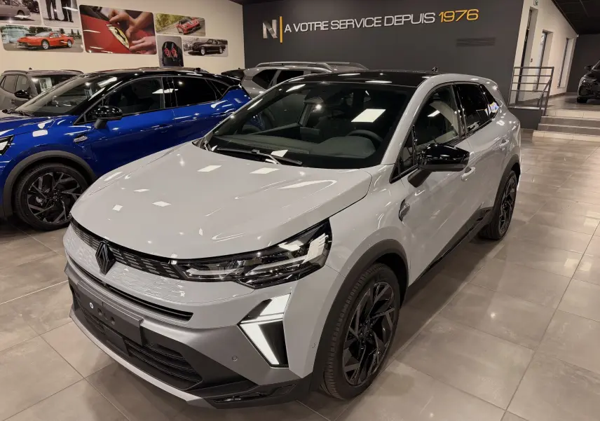 Renault Symbioz gris Rafale en 3/4 avant droit dans un showroom, avec jantes noires et éclairage LED distinctif.