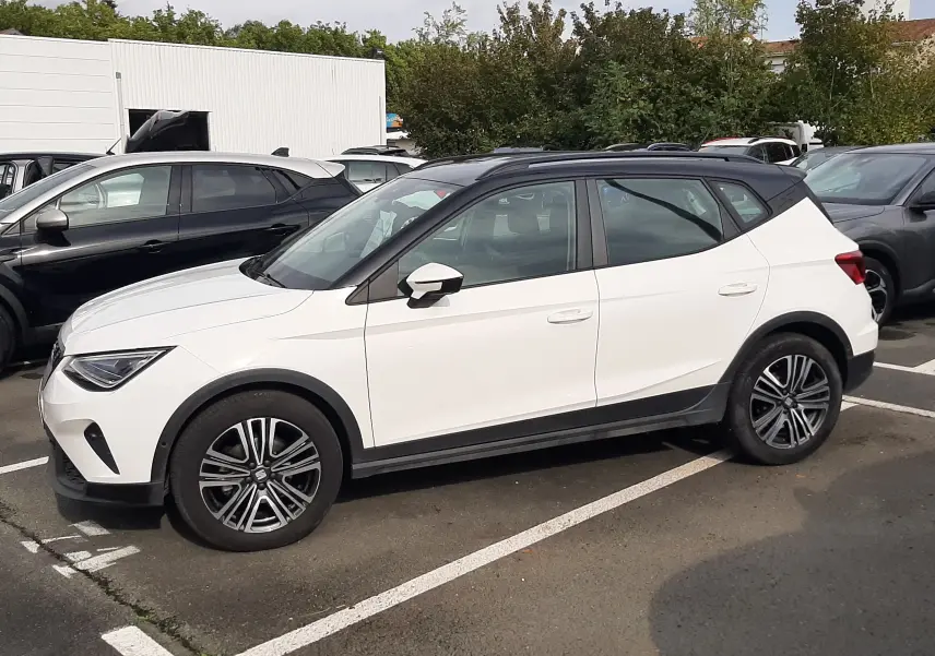 SEAT Arona 2024 blanc avec toit noir, vue de profil côté gauche, roues alliage et lignes modernes.