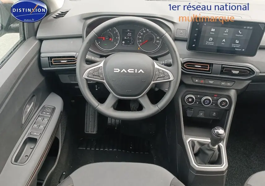Vue intérieure centrée sur le volant et la console centrale de la Dacia Sandero noire avec boîte manuelle et écran tactile.