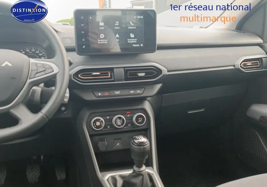 Vue intérieure côté conducteur du tableau de bord noir de la Dacia Sandero 2025 avec écran tactile et levier de vitesse manuel.