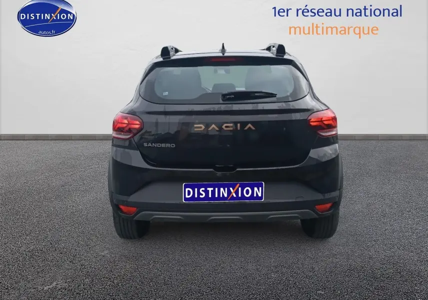 Vue arrière d'une Dacia Sandero noire 2025 avec feux arrière allumés et logo DACIA en relief cuivré.
