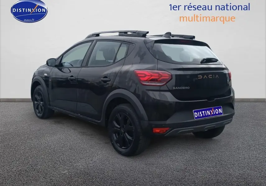 Vue 3/4 arrière droite d'une Dacia Sandero noire avec barres de toit et jantes alu noires.