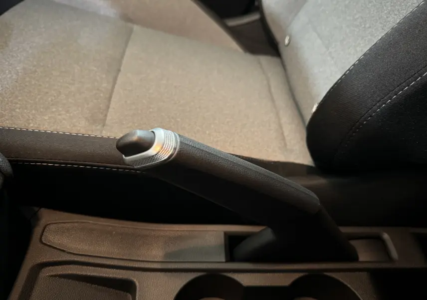 Le frein à main manuel en gros plan sur la console centrale, siège tissu gris clair de la Renault Clio.