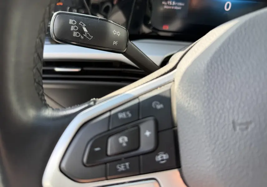 Gros plan sur la partie gauche du volant d’une Volkswagen Golf blanche 2020, avec commandes au volant et levier de clignotant.