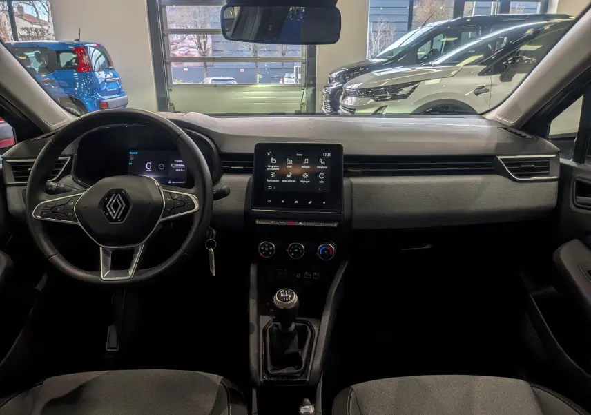 Vue intérieure avant de la Renault Clio V TCe 90 Evolution 2024, tableau de bord gris avec écran tactile et boîte manuelle.