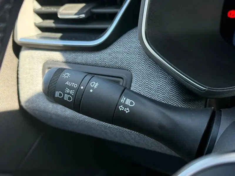 Gros plan sur la commande des feux et clignotants dans l’habitacle du Renault Clio 2025 avec motif tissu gris en arrière-plan.