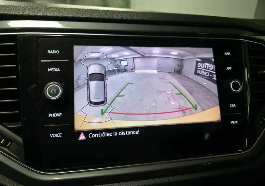 Écran tactile affichant la caméra de recul du Volkswagen T-Roc jaune avec repères de distance et vue aérienne du véhicule.