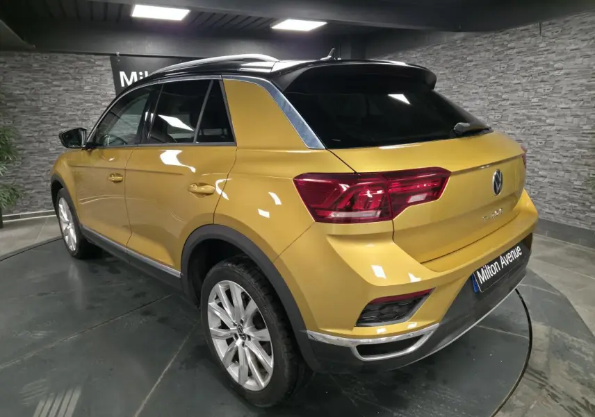 Vue 3/4 arrière droite d'un Volkswagen T-Roc jaune Curcuma avec toit noir et jantes alliage 18 pouces en intérieur showroom.