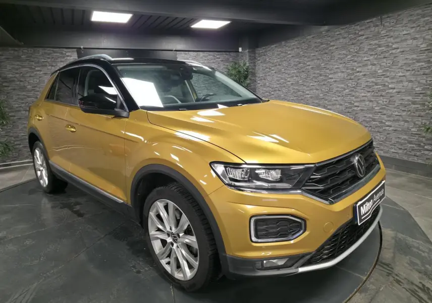 Volkswagen T-Roc jaune vue 3/4 avant droit, avec toit noir et jantes alliage 18 pouces en intérieur showroom.