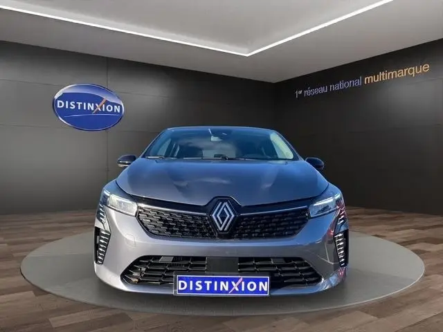 Vue frontale d'une Renault Clio Evolution TCe 90 gris foncé, avec calandre noire et feux LED allumés en intérieur showroom.