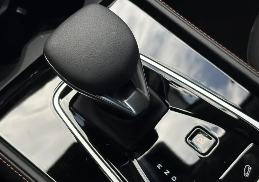 Gros plan sur le levier de vitesses automatique noir brillant de la MG MOTOR EHS 1.5 Hybrid+ 224 Luxury, intérieur noir.