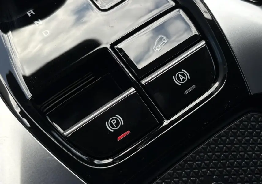 Gros plan sur la console centrale noire avec boutons de frein de stationnement et ouverture du hayon du MG Motor EHS blanc.