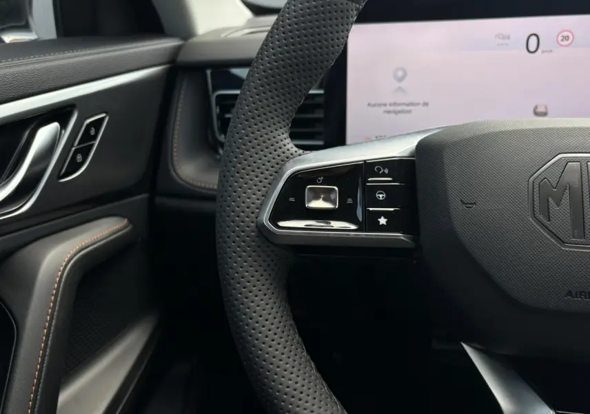 Gros plan sur le volant perforé noir du MG Motor EHS 1.5 Hybrid+ 224 Luxury avec tableau de bord numérique blanc en arrière-plan.