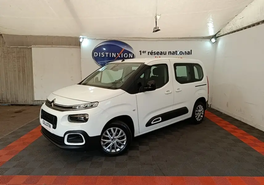 Vue 3/4 avant droite du Citroën Berlingo blanc avec protections latérales noires et jantes alliage en intérieur showroom.
