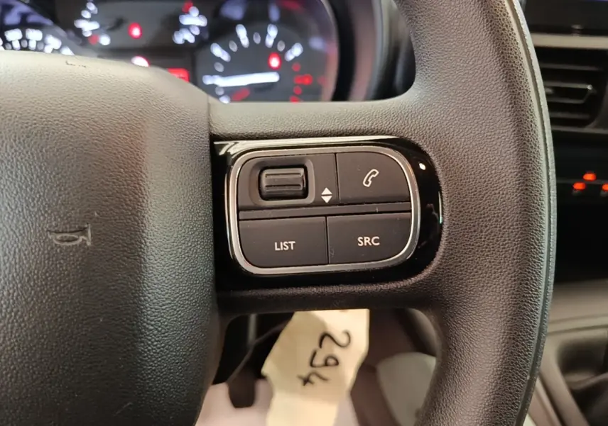 Gros plan sur le volant noir multifonctions du Citroën Berlingo blanc, avec commandes audio et téléphone visibles.