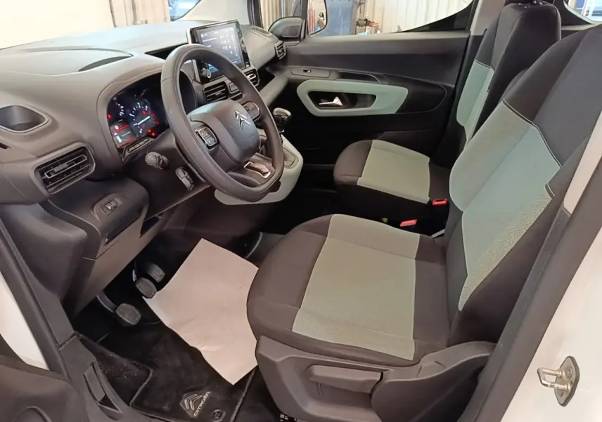 Vue intérieure côté conducteur du Citroën Berlingo blanc, montrant le volant multifonctions et les sièges bi-ton gris et noir.