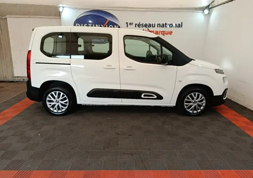 Profil droit d'un Citroën Berlingo blanc 2022 avec protections noires basses et jantes alliage en intérieur showroom.