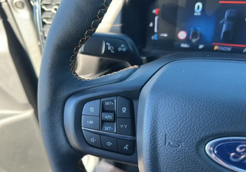 Gros plan sur le volant cuir du Ford Ranger gris carbone 2025, avec commandes multifonctions visibles à gauche.