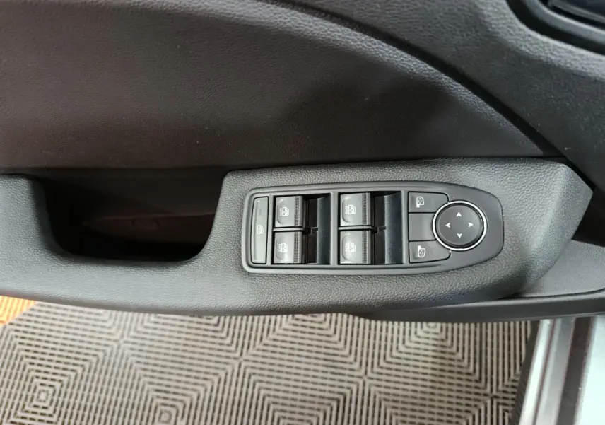 Vue rapprochée de la commande des vitres électriques et des rétroviseurs sur la porte côté gauche d'une Renault Clio gris clair 2025.