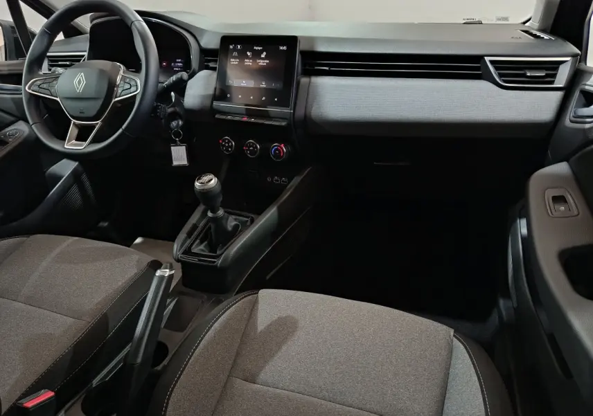Vue intérieure avant de la Renault Clio 2025, tableau de bord gris clair avec écran tactile central et volant cuir multifonctions.