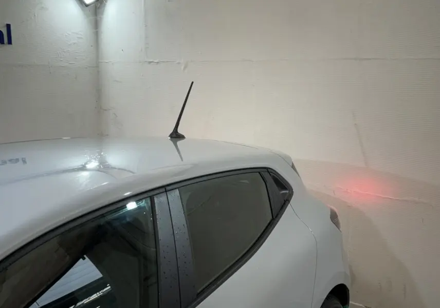 Vue 3/4 arrière droite d'une Renault Clio gris clair avec antenne de toit et vitres teintées dans un garage.