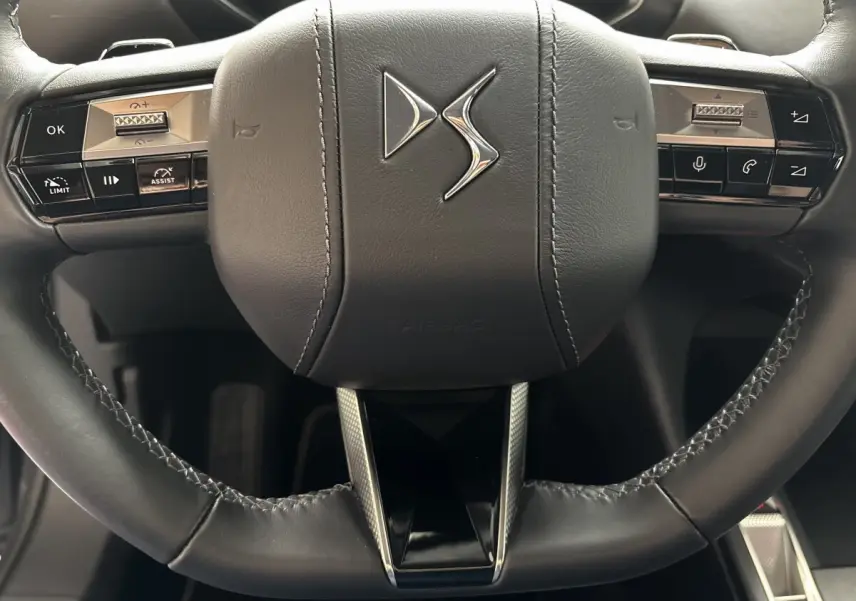 Gros plan sur le volant cuir noir du DS3 2024 avec commandes multifonctions et logo DS central argenté.