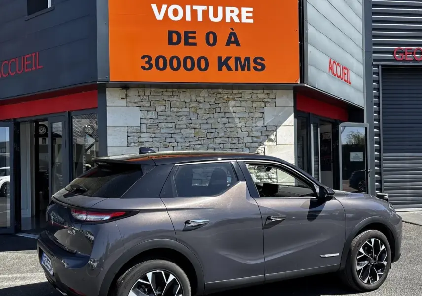 Vue 3/4 arrière droite d'une DS3 1.2 PureTech 130 Auto Esprit de Voyage gris foncé avec jantes noires et toit noir.